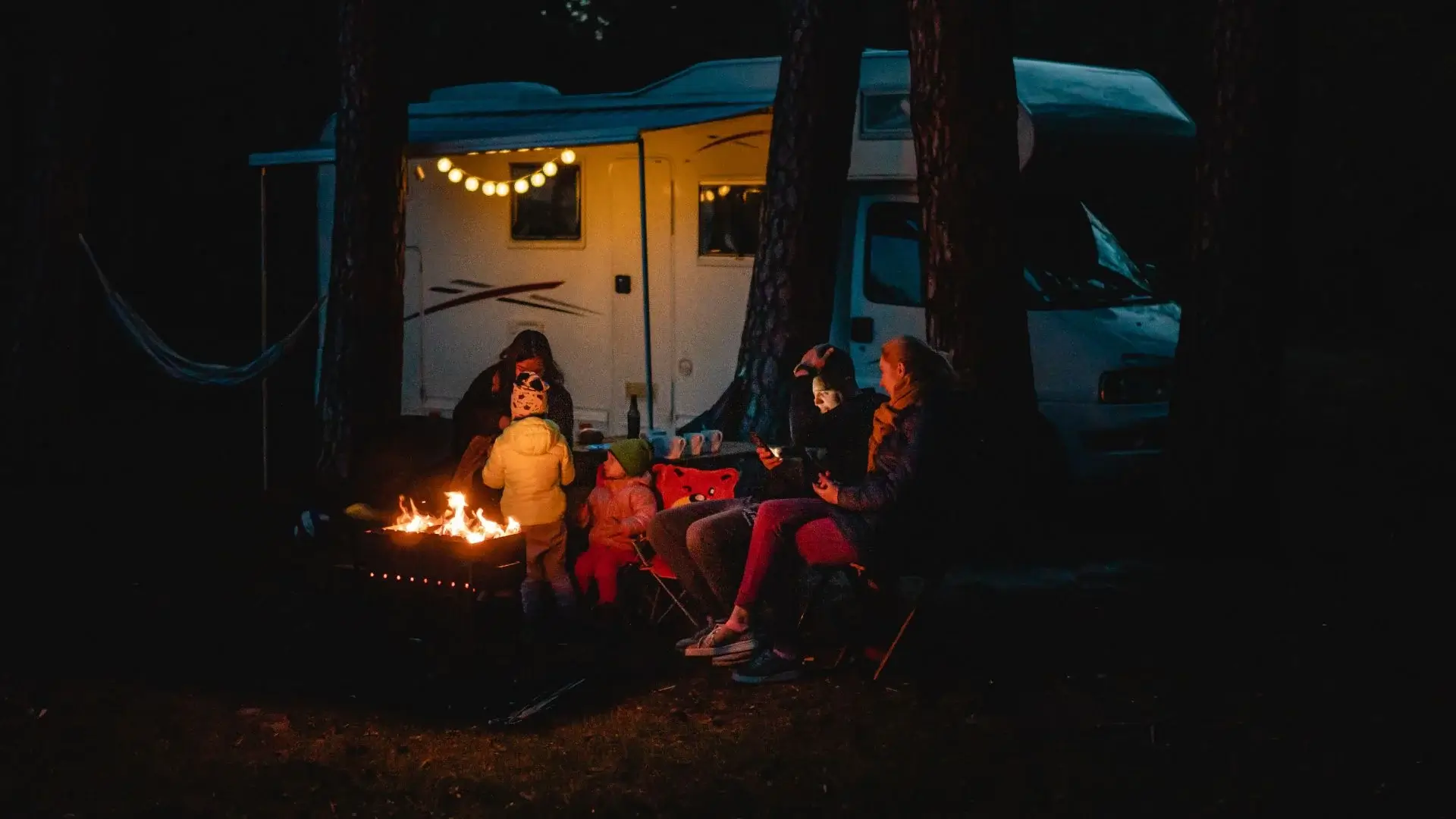 Family by campfire outside RV at night
