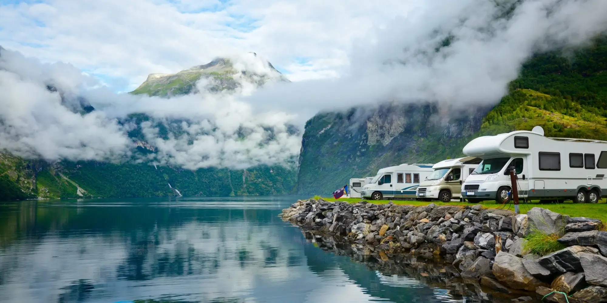 RVs by a fjord with mountains and clouds